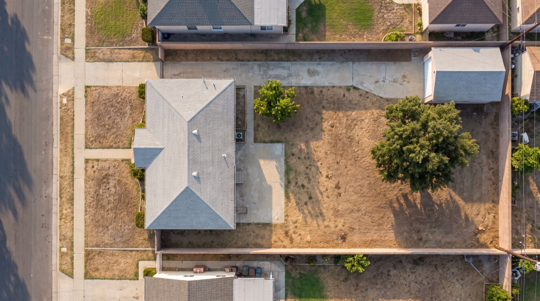 Top-down drone view of a San Fernando Valley house with a large backyard, an old detached garage and a big tree